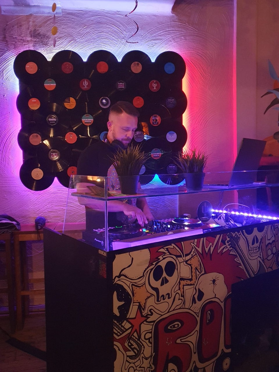 Sebastian legt im Club vor einer magenta hinterleuchteten Schallplattenwand auf