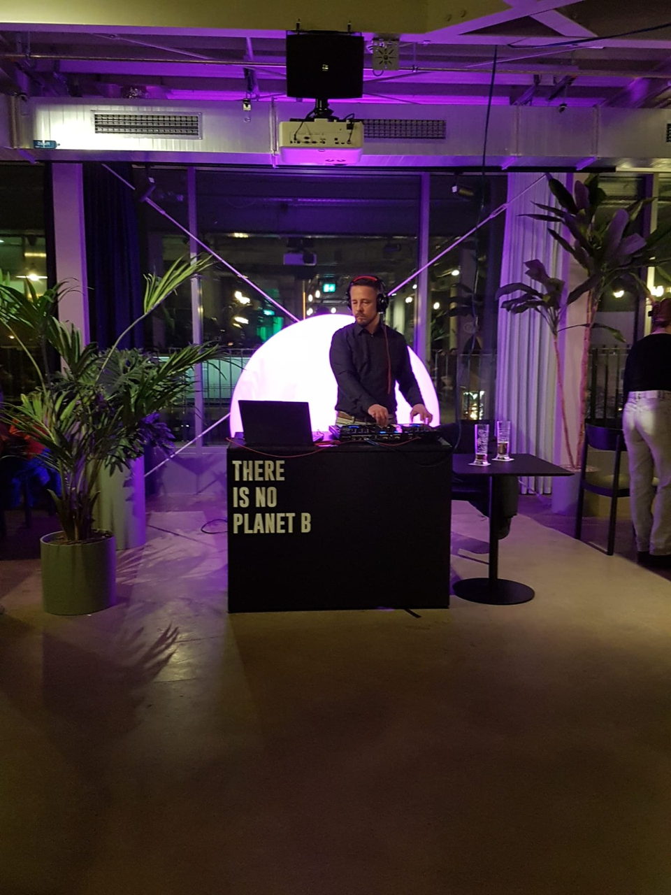 Sebastian am DJ-Pult vor einer magenta leuchtenden Kugel bei einem Firmenevent mit Blick über die Stadt
