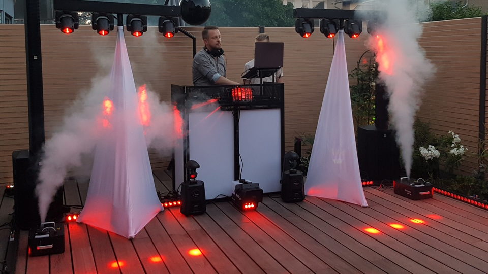 DJ-Aufbau mit Lichtstativen, rotem Licht und Nebelmaschinen auf einer Holzterrasse bei einer privaten Feier