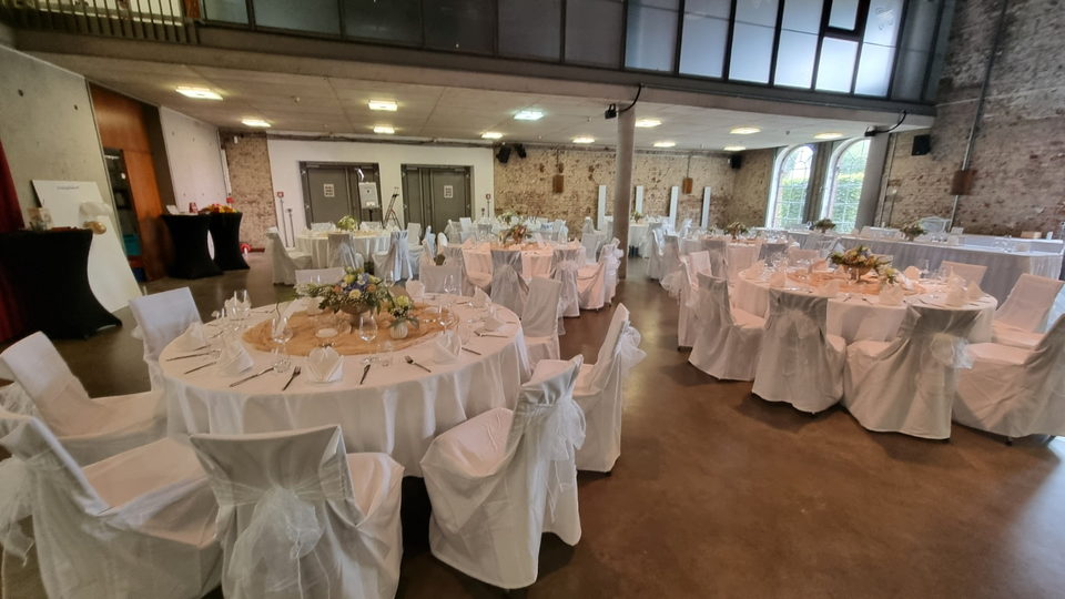 Festlich eingedeckter Hochzeitssaal mit runden Tischen, weißen Stuhlhussen und Blumengestecken