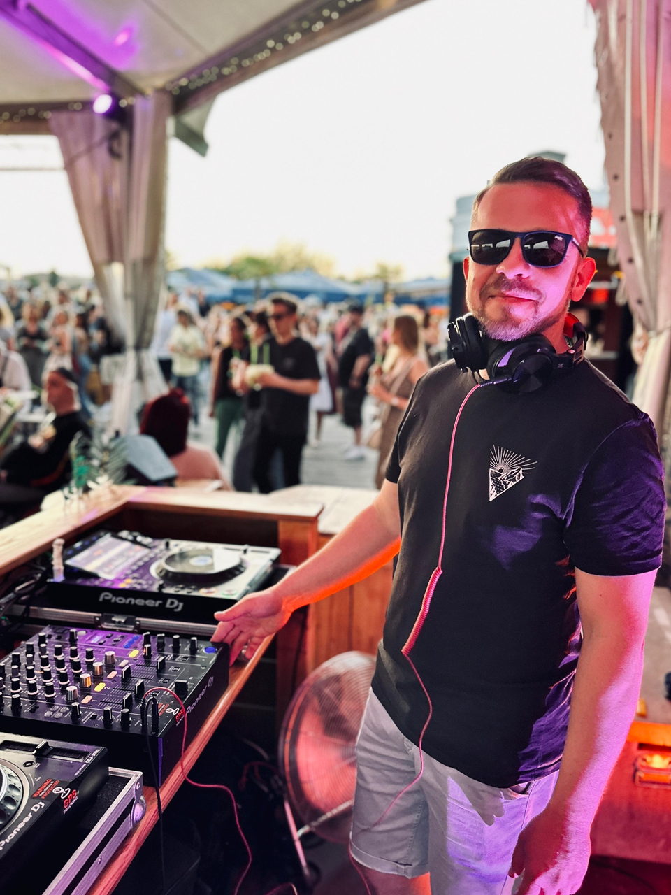 Sebastian mit Sonnenbrille und Kopfhörern am Pioneer-Pult, dahinter Gäste bei einem Sommerfest